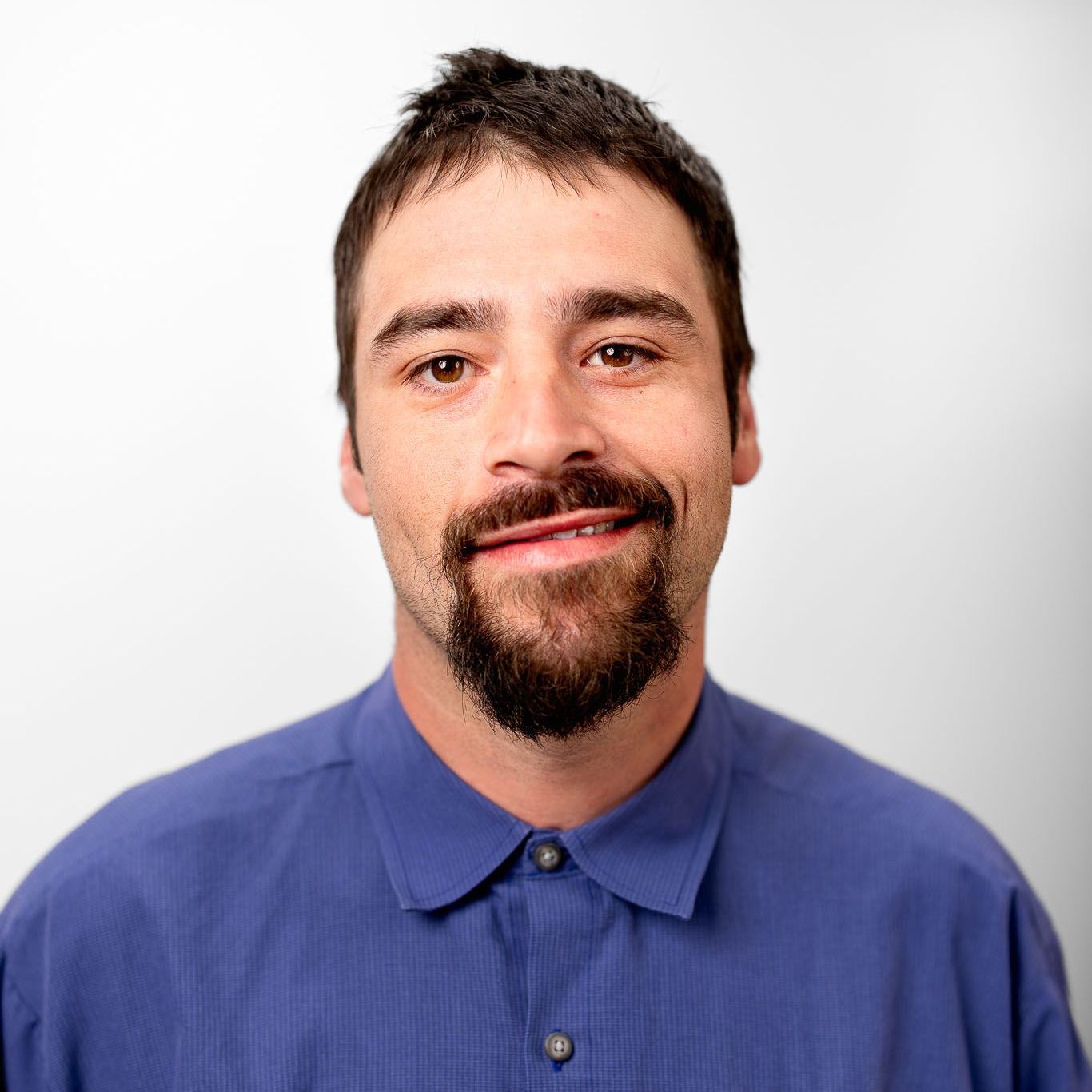 A man with a beard is wearing a blue shirt and smiling for the camera.