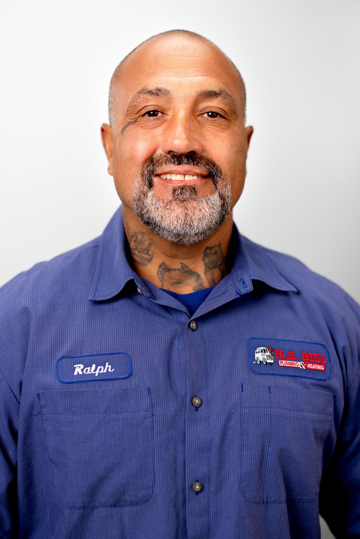 Man with shaved head and beard in blue  R.A. Biel work shirt, smiling for headshot for photo