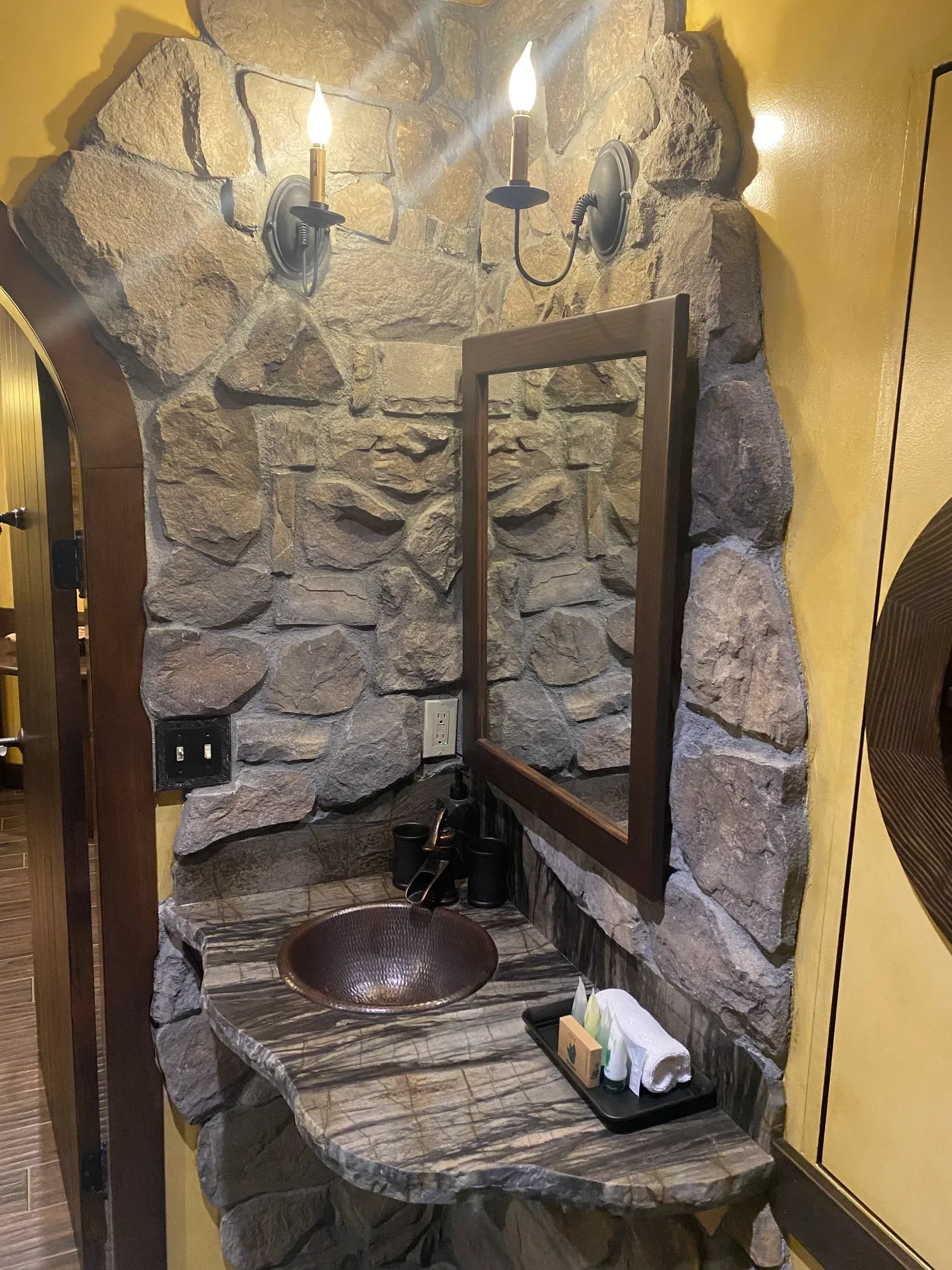 A bathroom with a stone wall , a sink and a mirror.