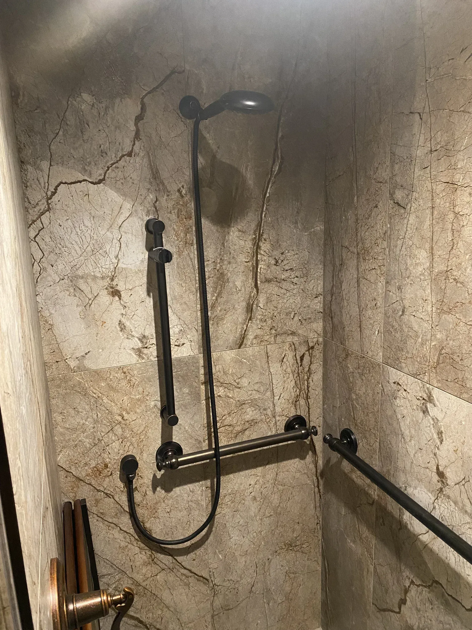 A bathroom with a shower head and a hand rail.