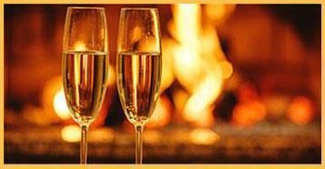 Two glasses of champagne are sitting in front of a fireplace.