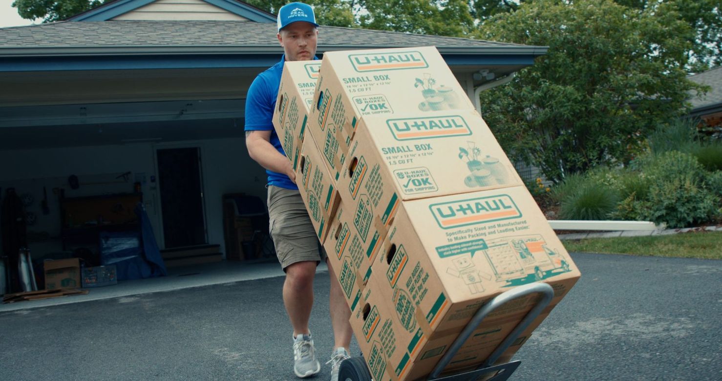 A man is pushing a cart full of boxes in front of a house.