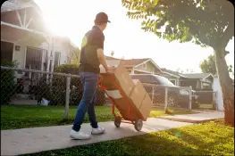 A delivery man is pushing a cart with boxes on it down a sidewalk.