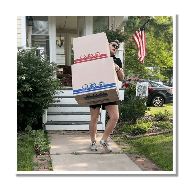 A man is carrying two boxes in front of a house.