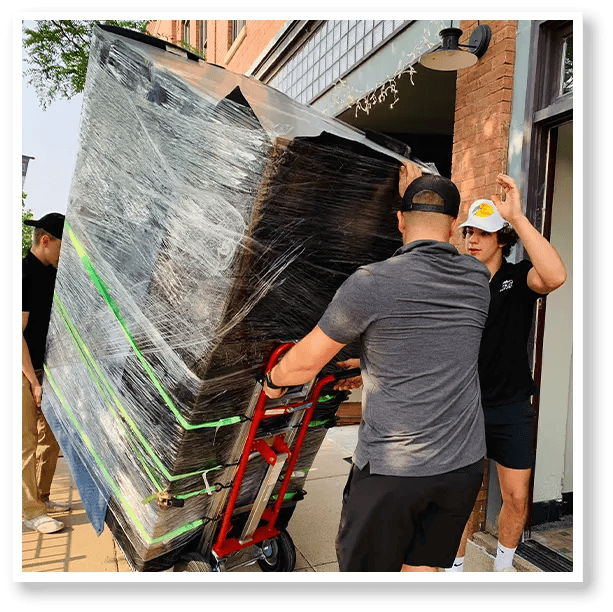 Two men are carrying a large piece of furniture on a dolly.