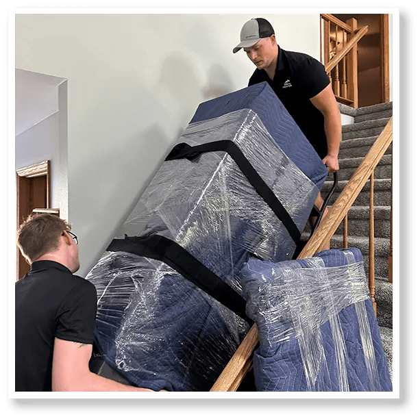 Two men are carrying a couch up a set of stairs.