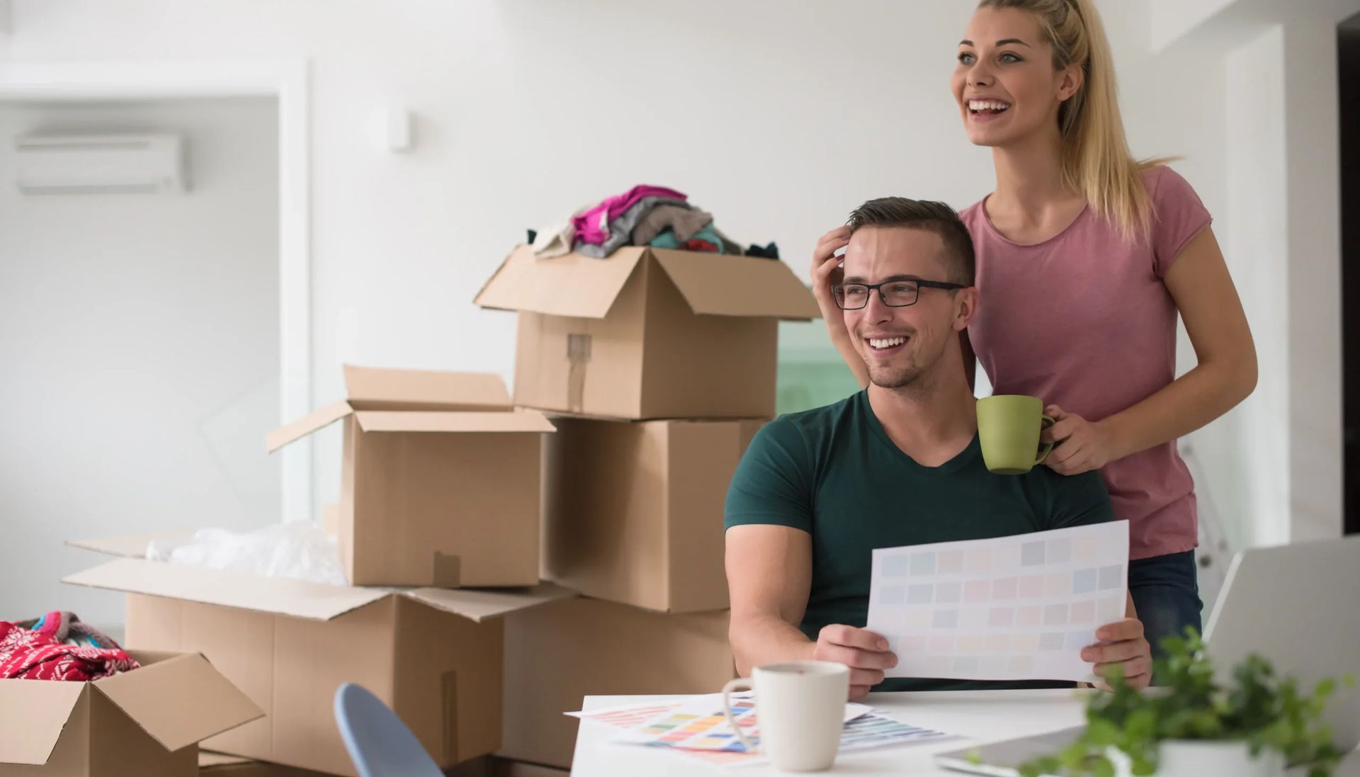 A man and a woman are sitting at a table in front of a pile of cardboard boxes.