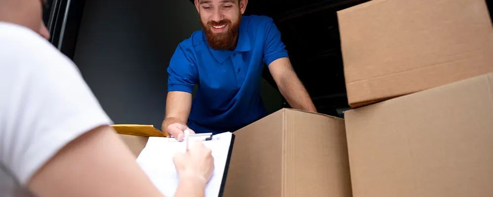 A delivery man is giving a box to a woman who is holding a clipboard.