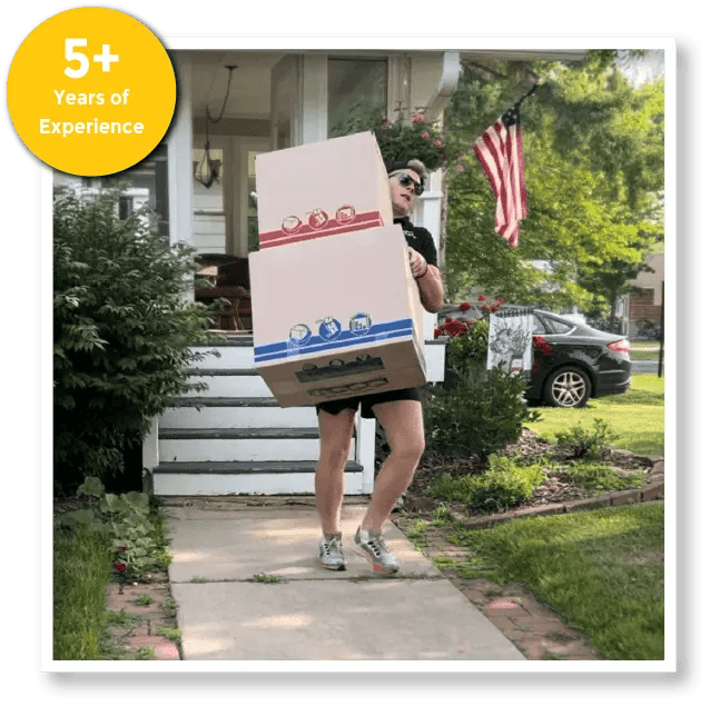 A man is carrying a stack of boxes in front of a house.