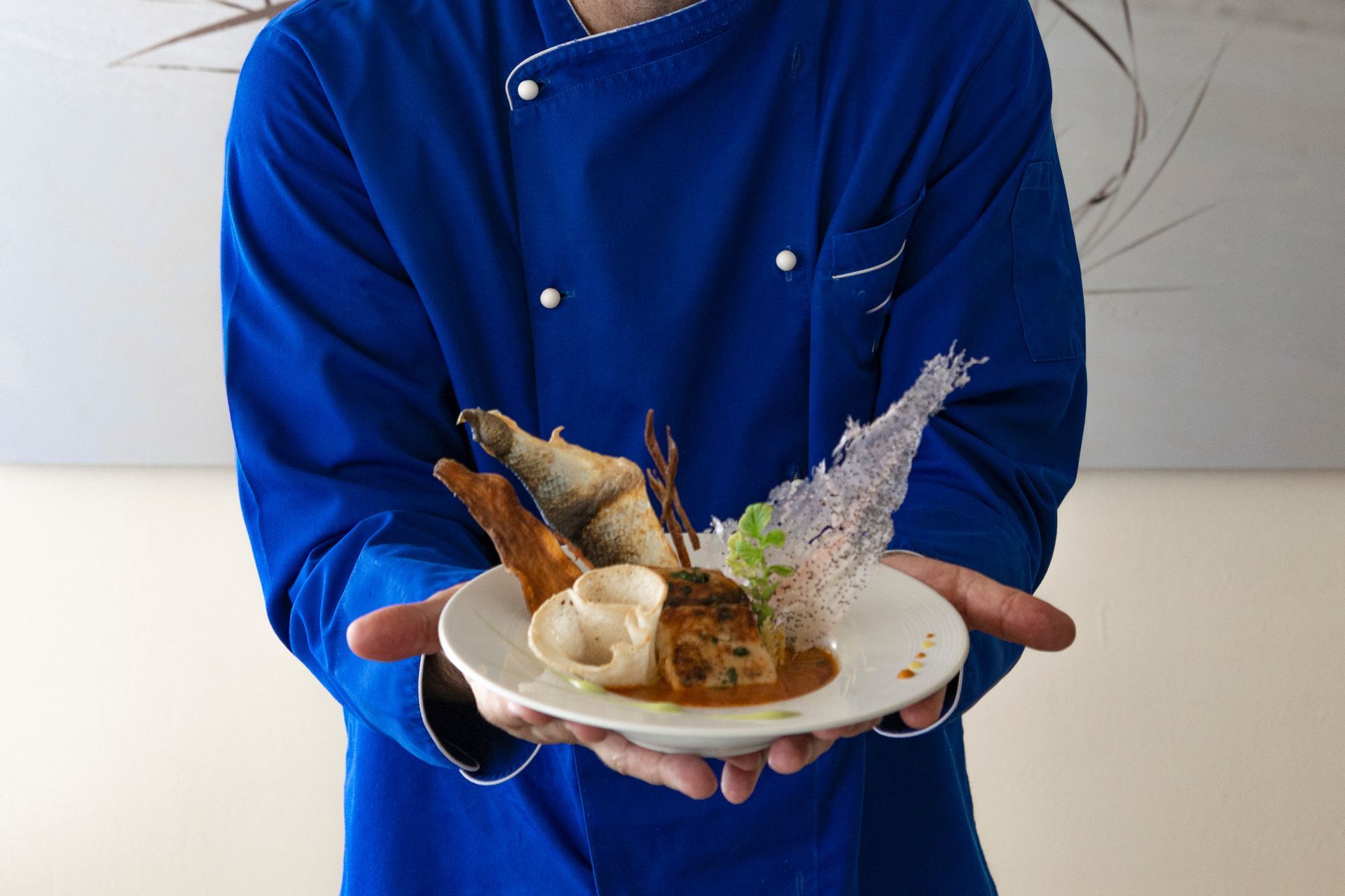 Chef in blue coat presenting a plate of garnished food.