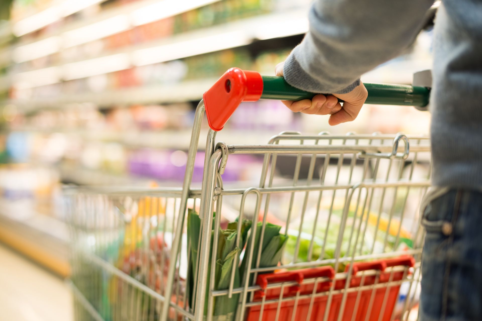 Person pushing a shopping cart through a supermarket aisle filled with products.