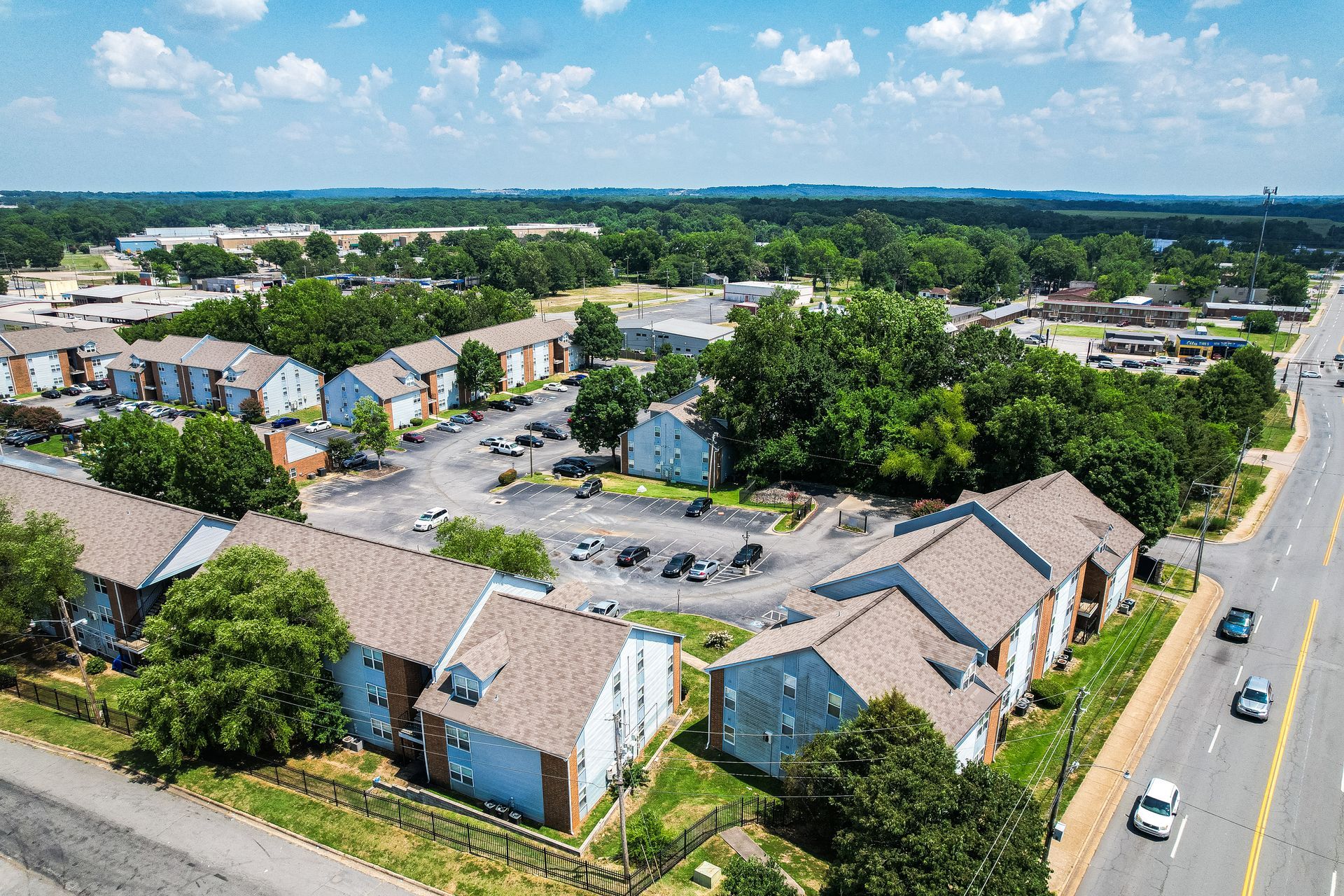 Aerial view of a residential complex with multiple buildings, a circular parking lot, and a road with passing cars.