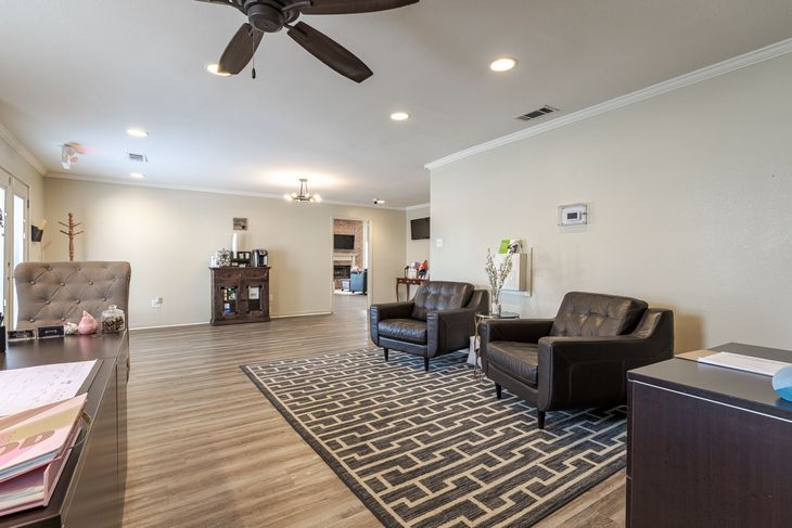 Spacious waiting room with brown leather armchairs, patterned rug, dark wood desk, and ceiling fan.