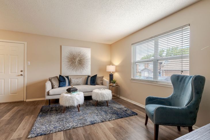 Living room with couch, teal chair, and window with blinds; beige walls, wood floors.