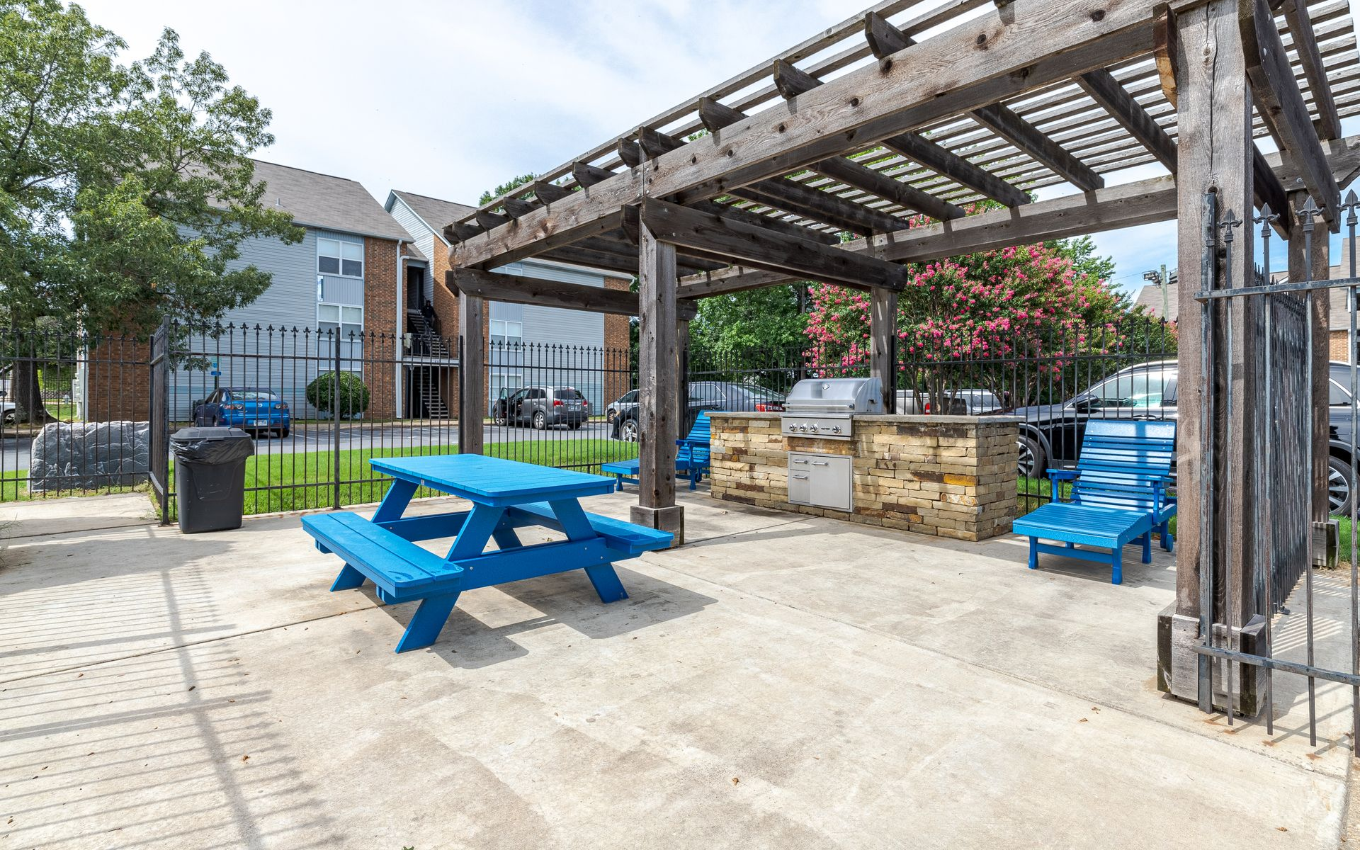 Outdoor picnic area with blue picnic table, grill, and pergola.