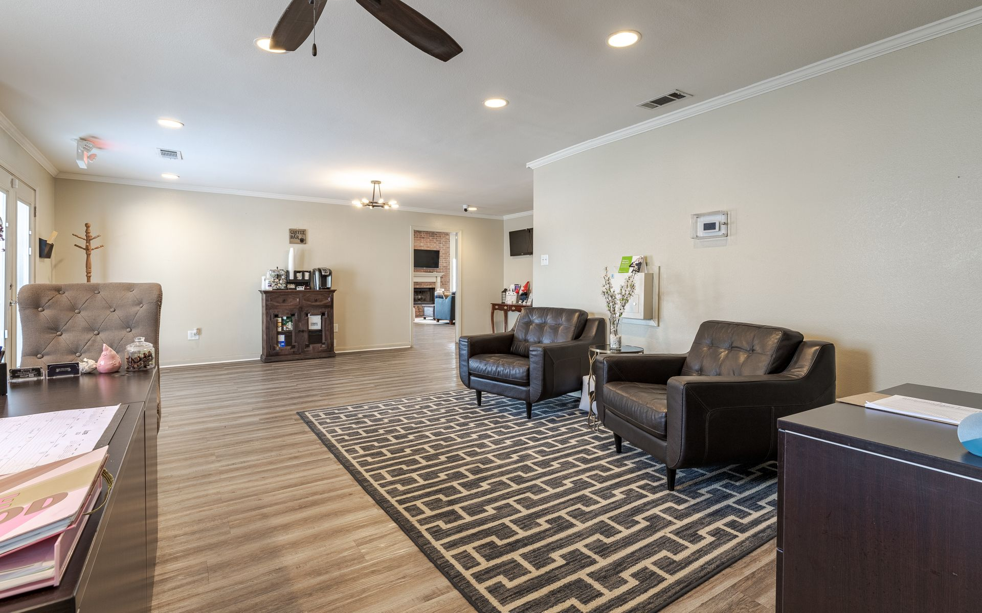 Spacious waiting room with brown leather armchairs, patterned rug, dark wood desk, and ceiling fan.