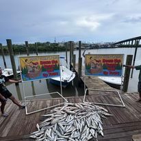 Two men are standing on a dock next to a pile of fish.