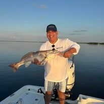 A man is standing on a boat holding a large fish.