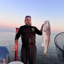 A man is standing on a boat holding a large fish.