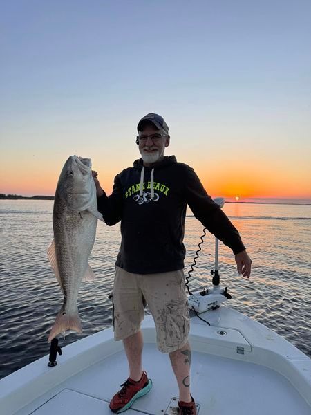 A man is standing on a boat holding a large fish.