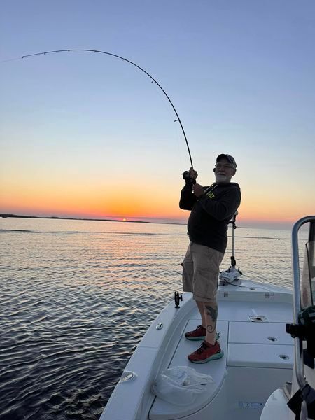 A man is fishing on a boat in the ocean at sunset.