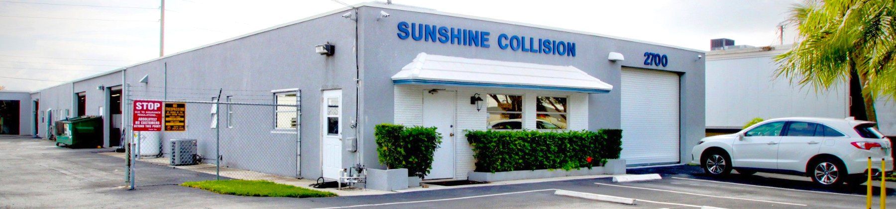 A white car is parked in front of a building that says sunshine cleaner.