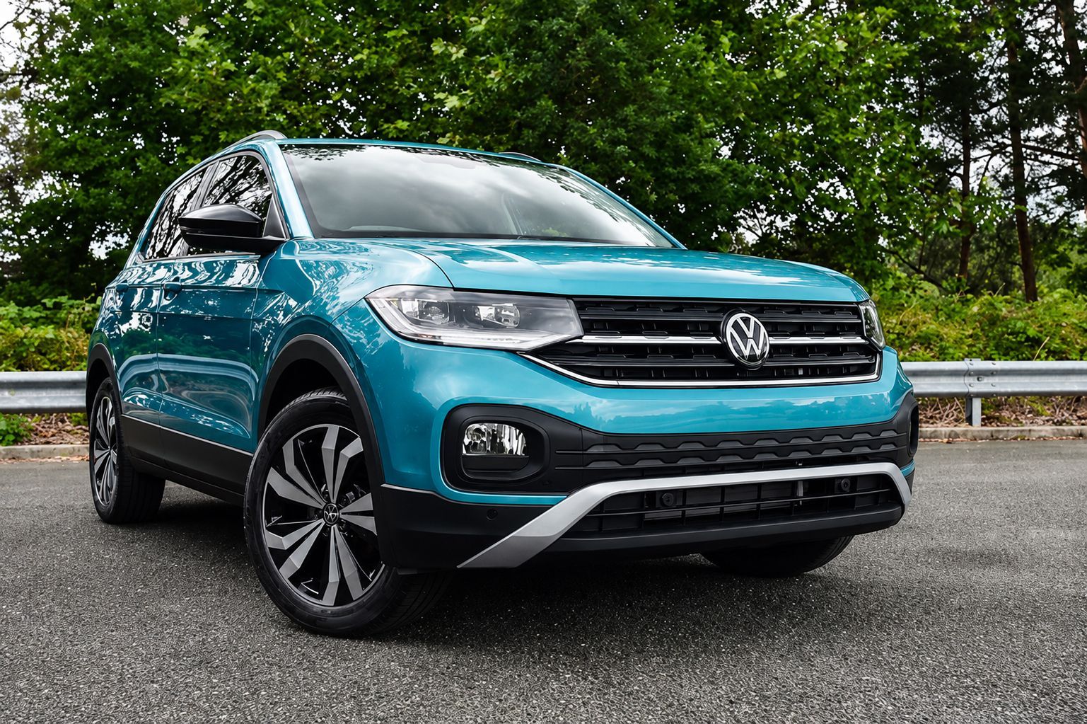 Teal Volkswagen SUV parked on a road with trees and a guardrail in the background