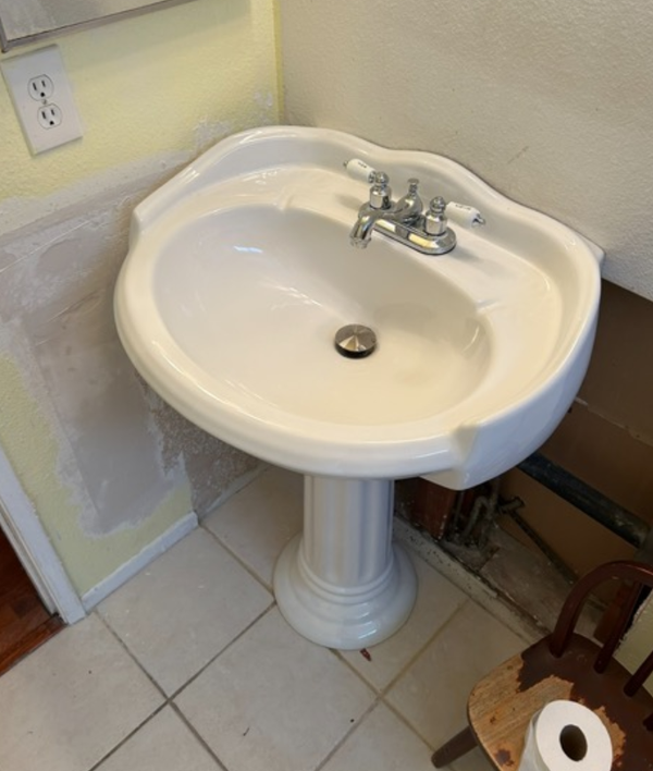 A white pedestal sink in a bathroom next to a chair