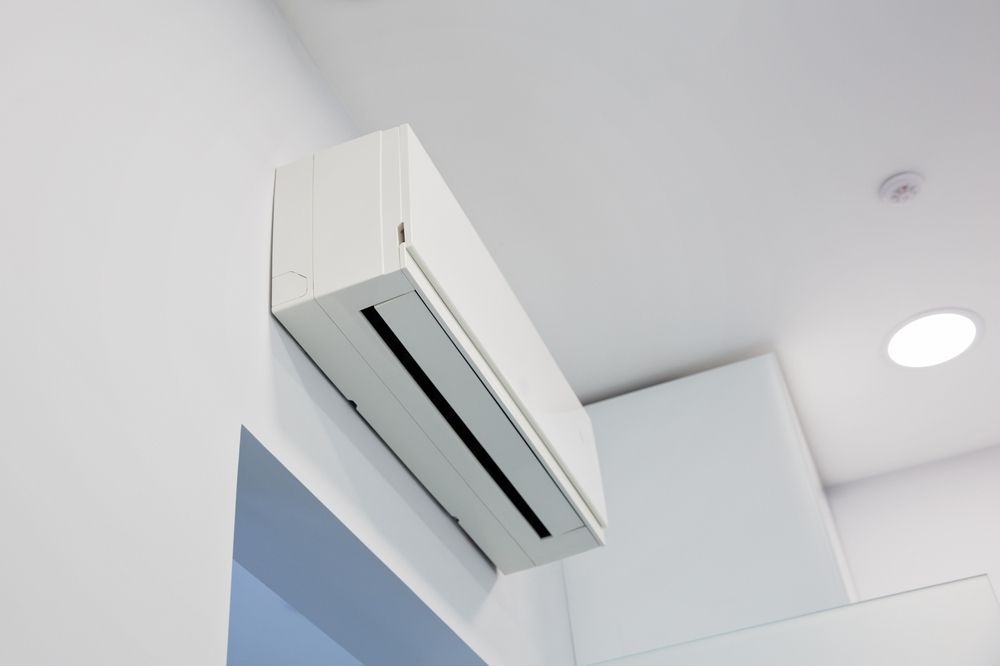 A white split-system air conditioner mounted on a white wall in a room with a ceiling light.
