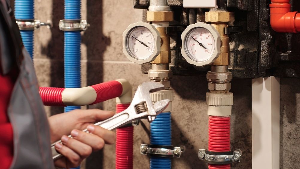 A technician uses an adjustable wrench to work on pressurized pipes and gauges in a utility room.