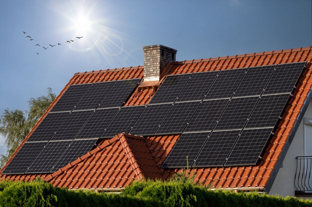 Solar panels installed on a residential home's tiled roof against a sunny, blue sky with birds flying overhead.