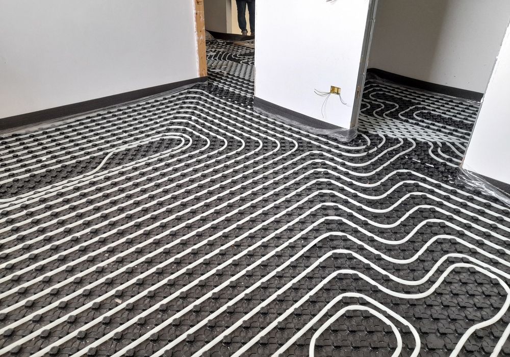 White underfloor heating pipes installed in a grid pattern across a room with a black knobbed subfloor base.