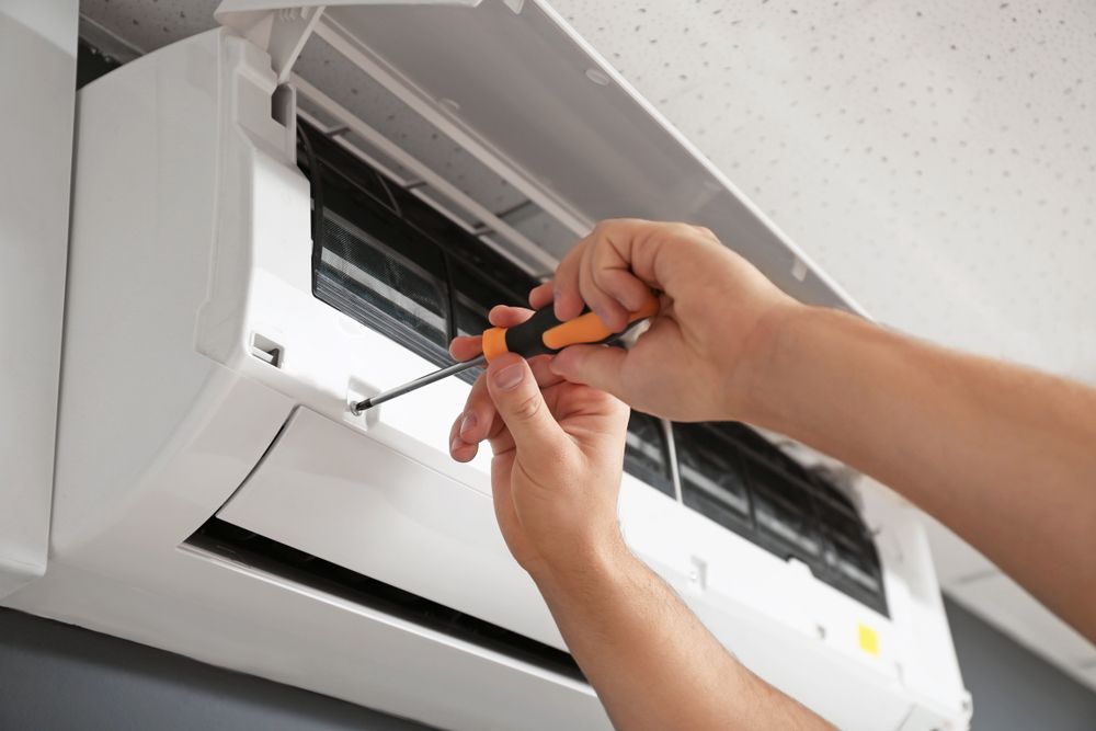 A person uses a screwdriver to service the interior components of a white wall-mounted air conditioner.