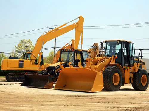 Yellow construction vehicles parked on dirt lot.