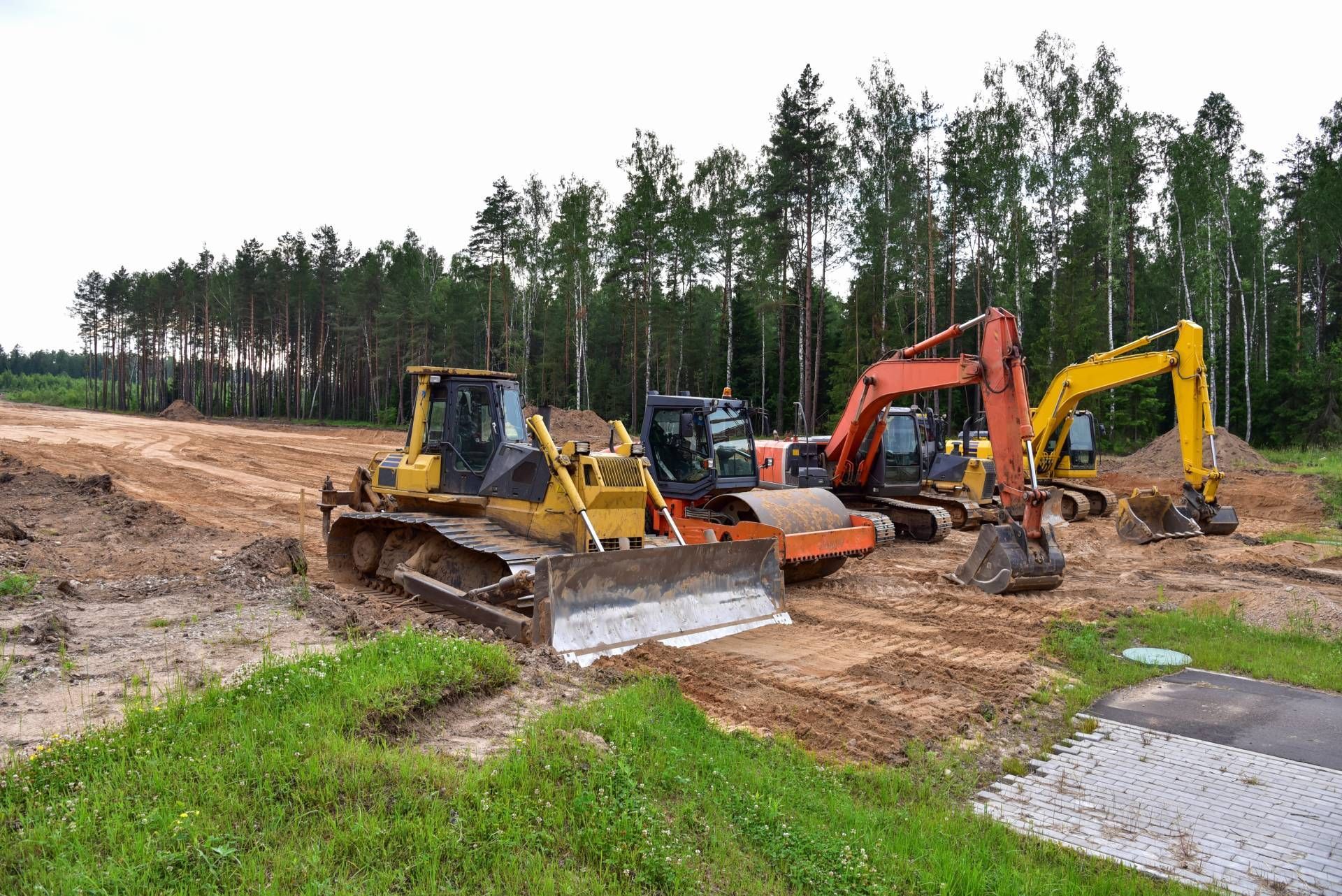 Bulldozer, excavator, and other construction equipment on dirt, in a forest clearing.