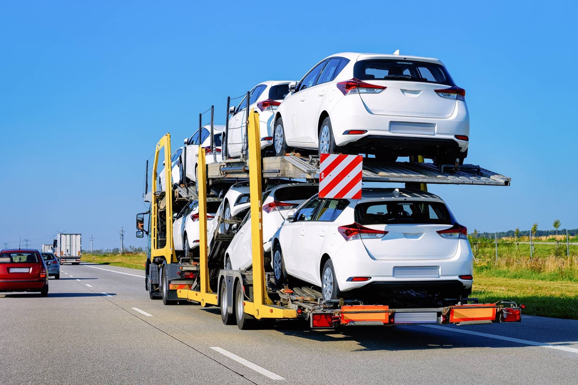 Car carrier truck transporting white vehicles on a highway under a clear blue sky.