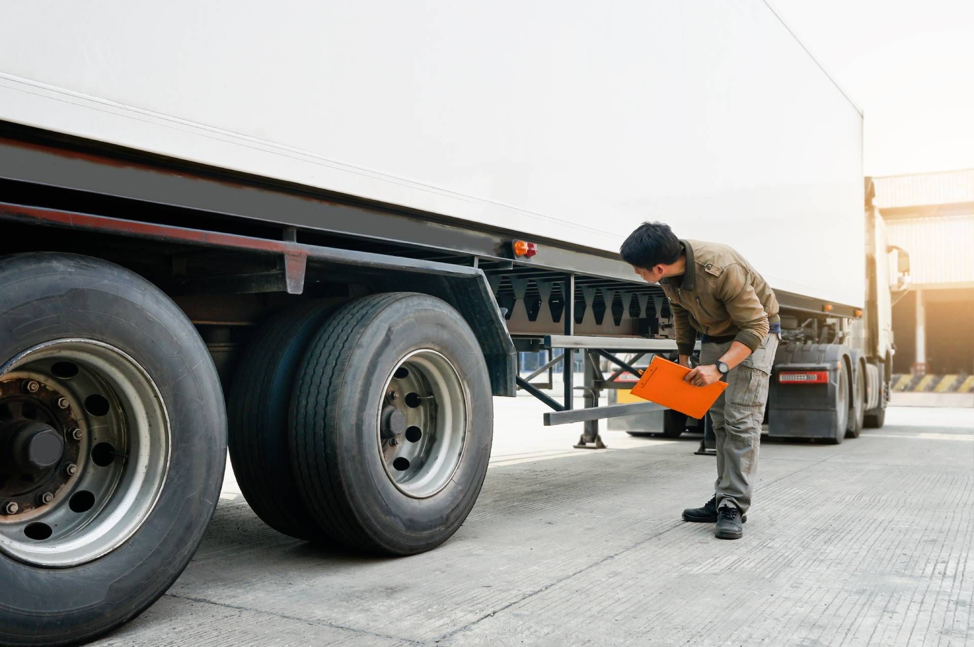 A person inspecting the wheels of a semi-truck, holding a clipboard outdoors.