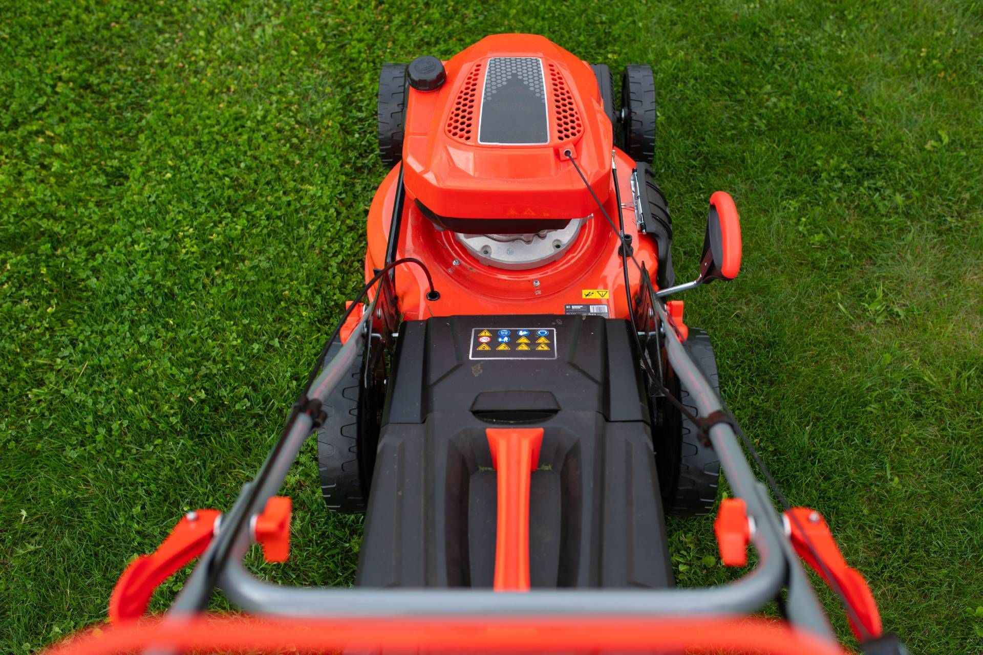 Orange and black lawnmower on green grass, viewed from above, ready for mowing.