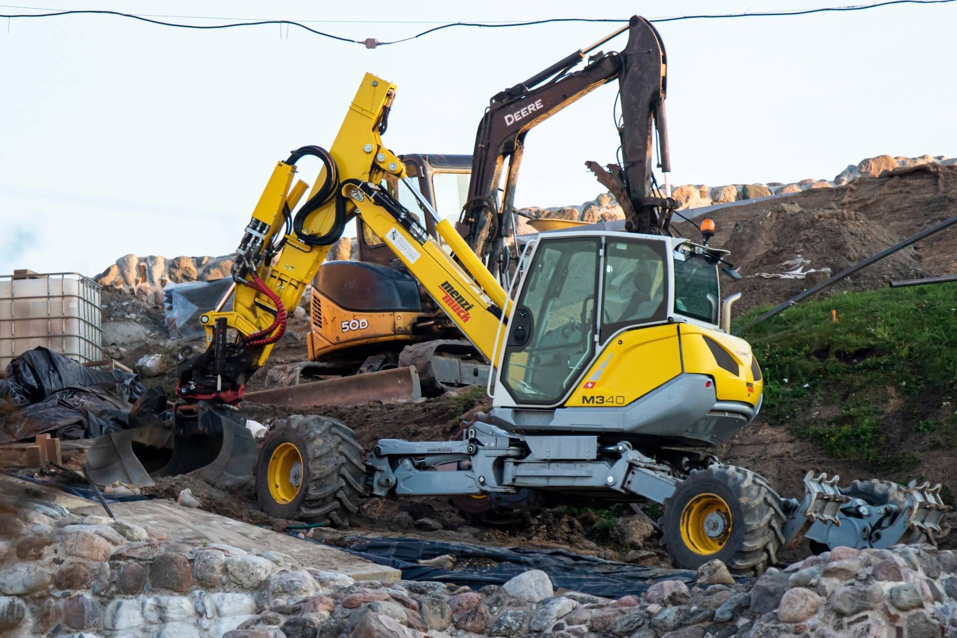Yellow excavator and dark excavator on construction site.
