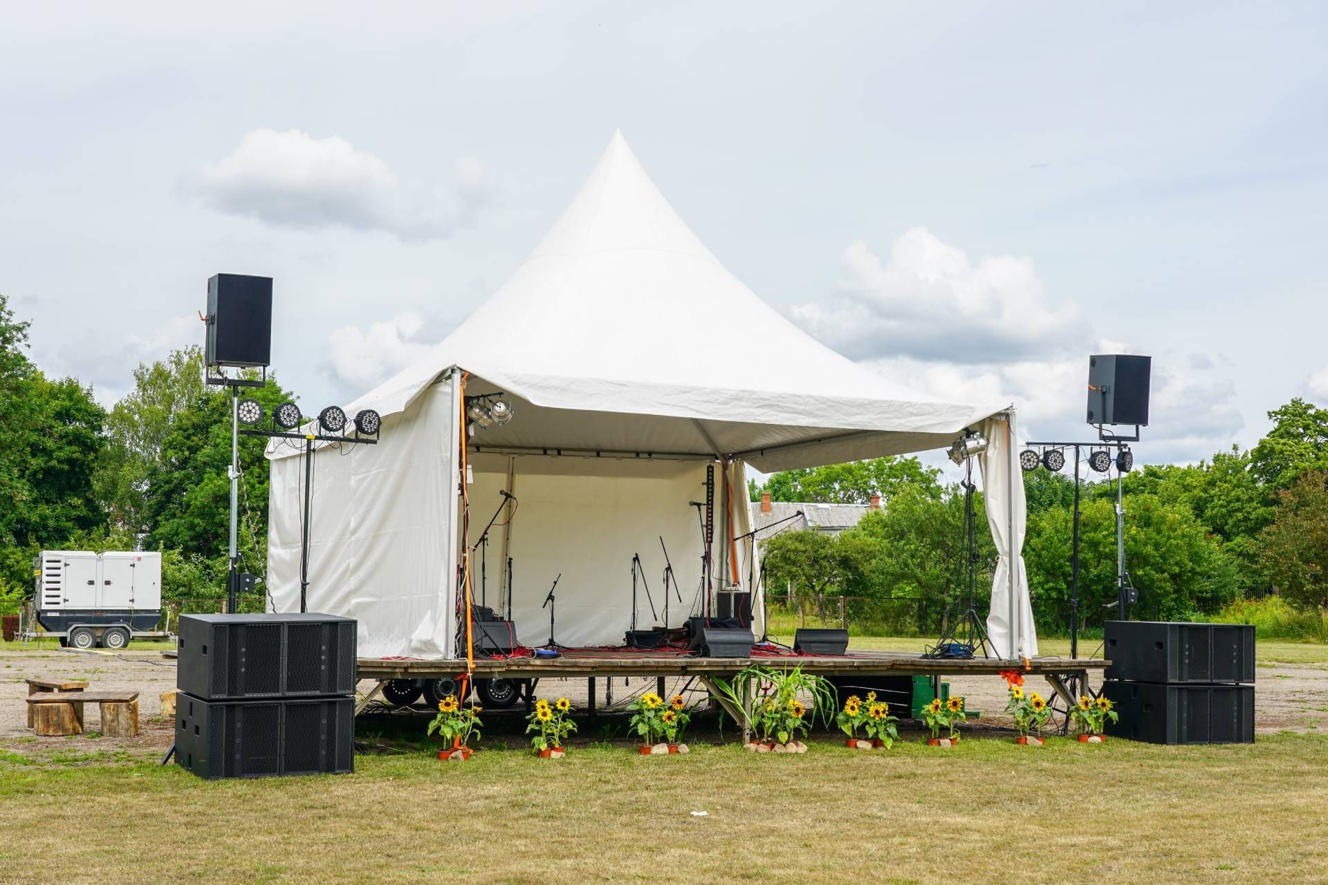 Outdoor stage with white tent, speakers, and microphones set up on grass.