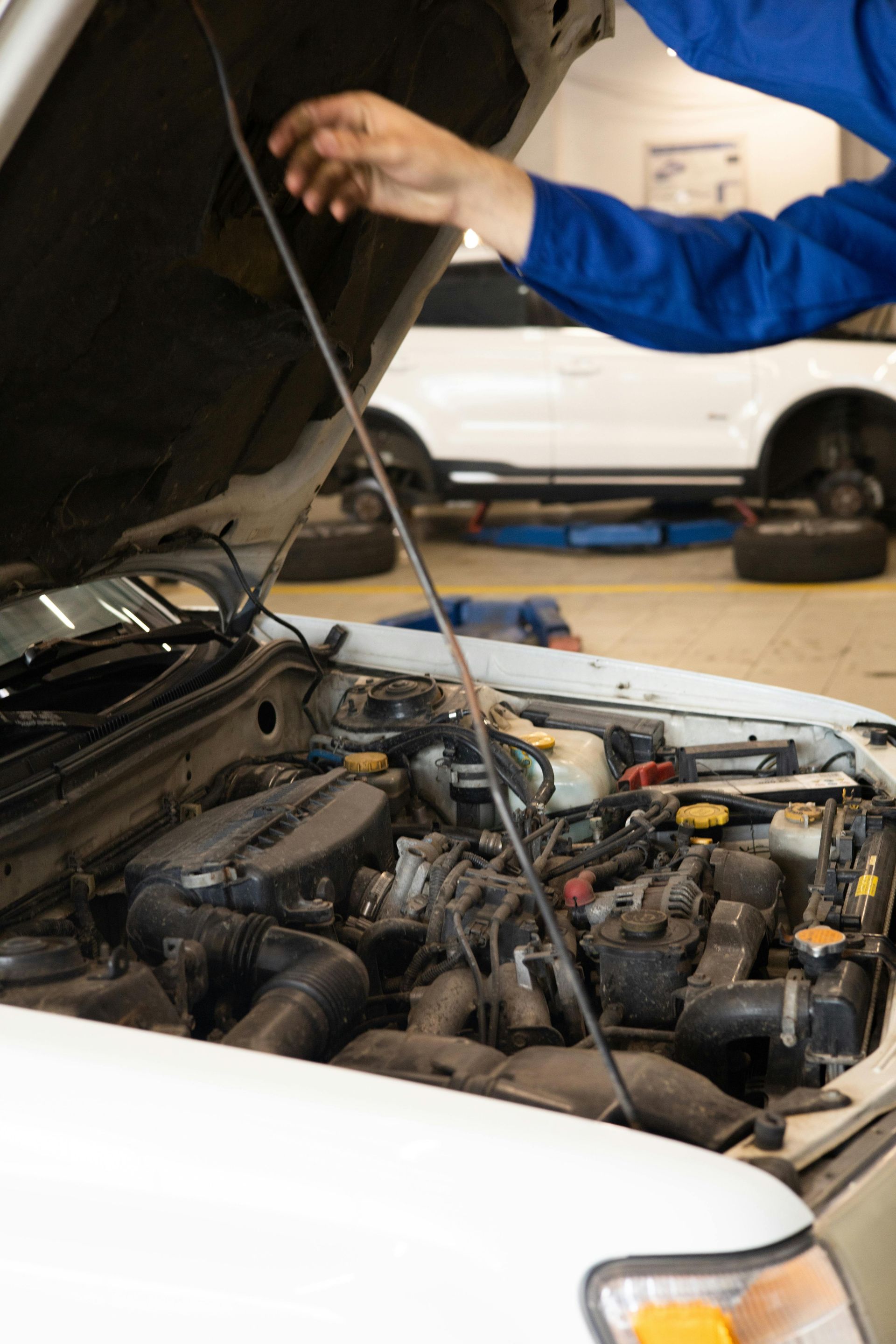 Mechanic in blue overalls working on a car engine in a garage.