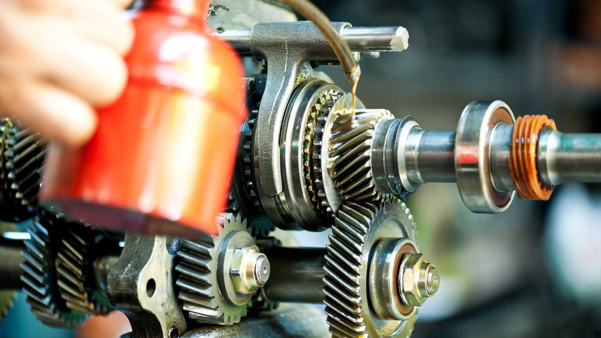 Gears being lubricated with oil from a red can; machinery, close-up.