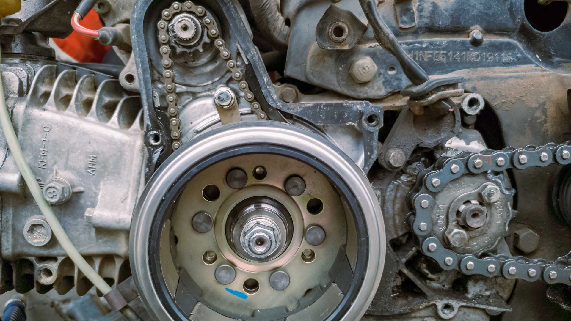Close-up of motorcycle engine components: chain, sprocket, and flywheel.