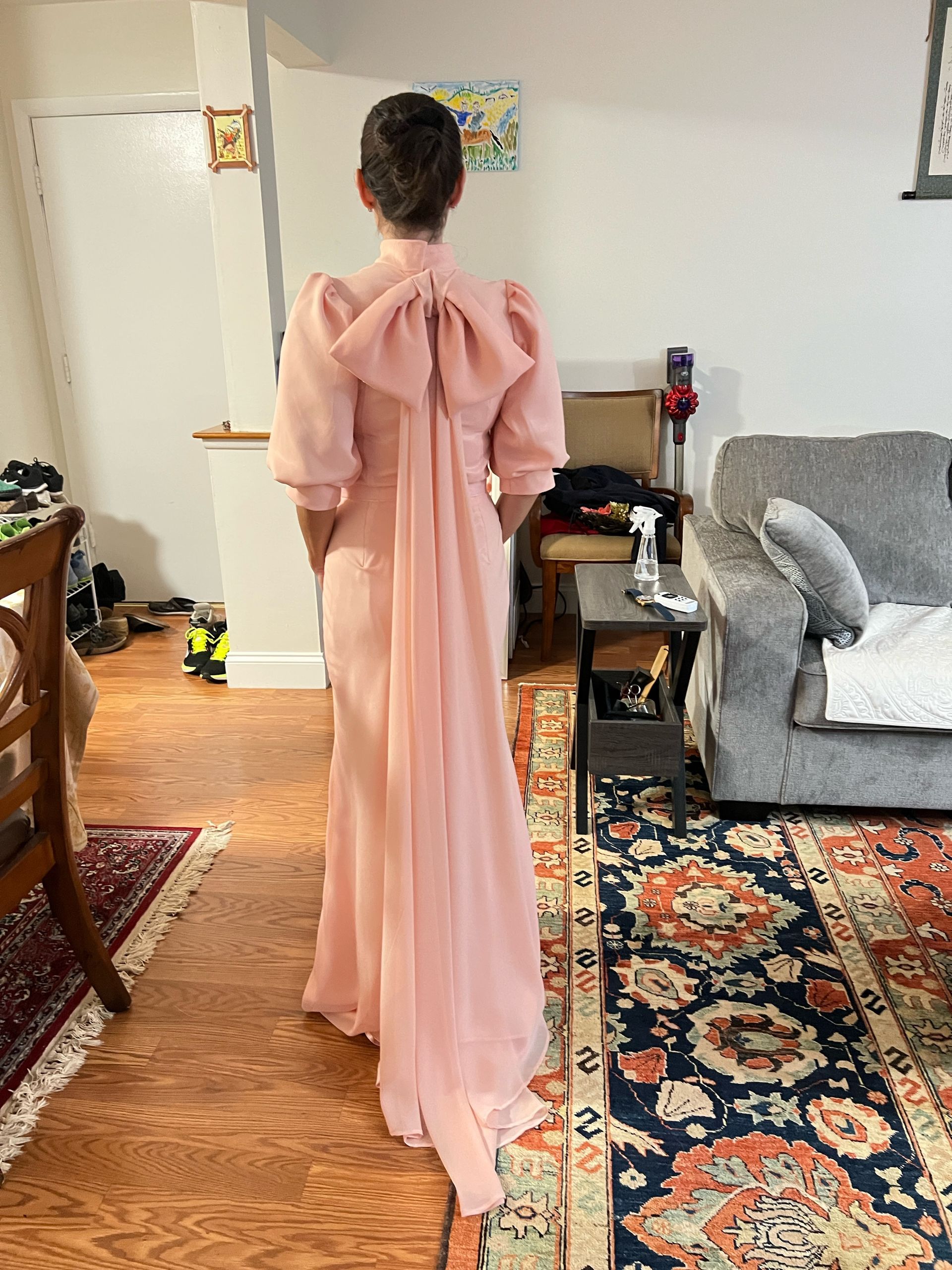 Woman in pink gown with bow and train, standing indoors.