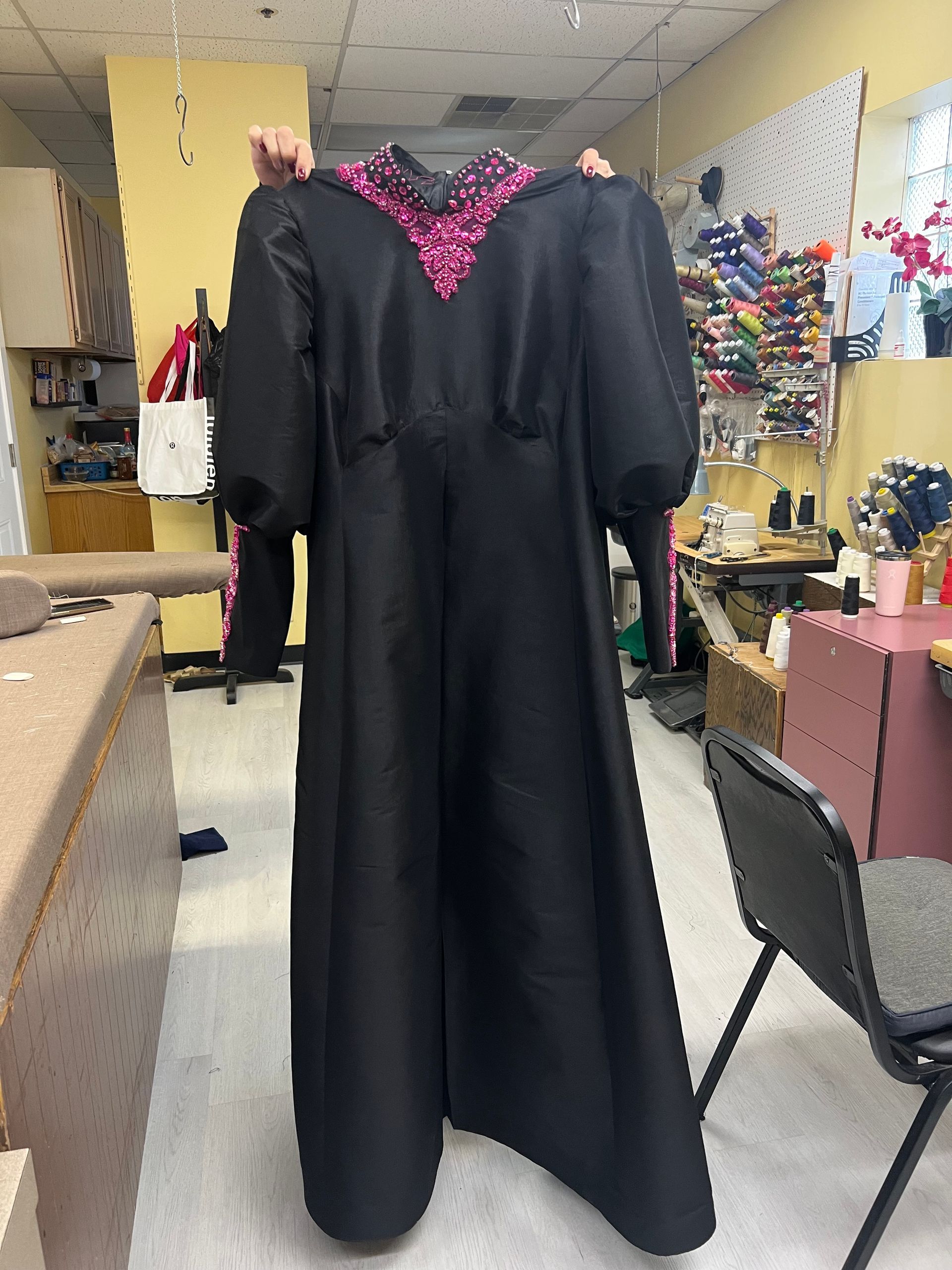 Tailor measuring a man's shoulders for a suit fitting. White measuring tape and collar visible.