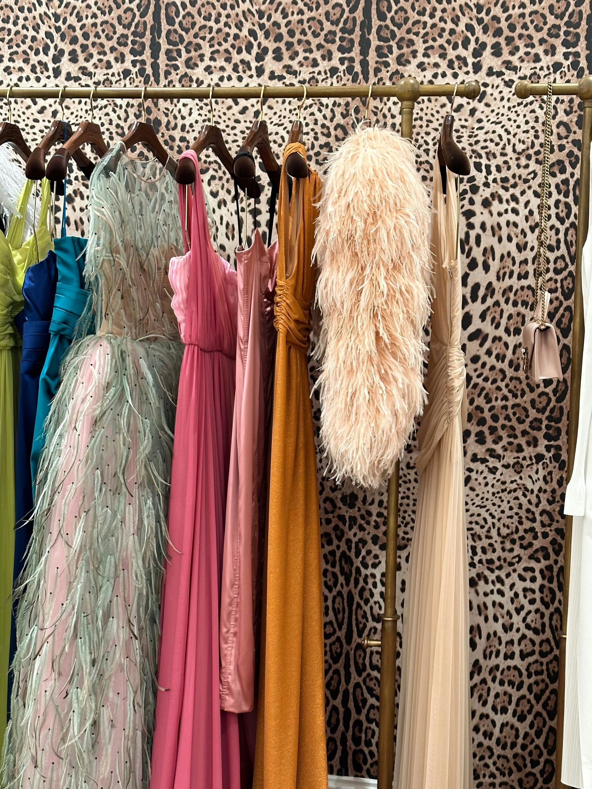 Rack of colorful formal dresses in front of a leopard-print wallpaper.