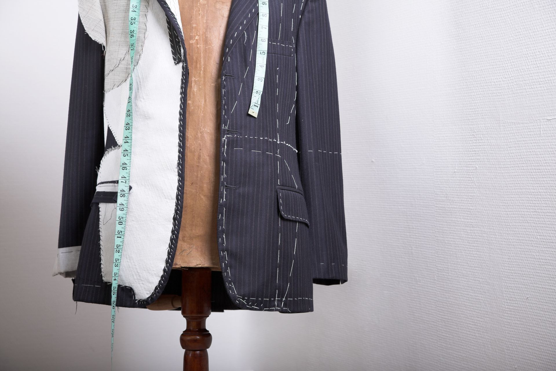 Tailor's mannequin with partially sewn suit jacket and measuring tape.