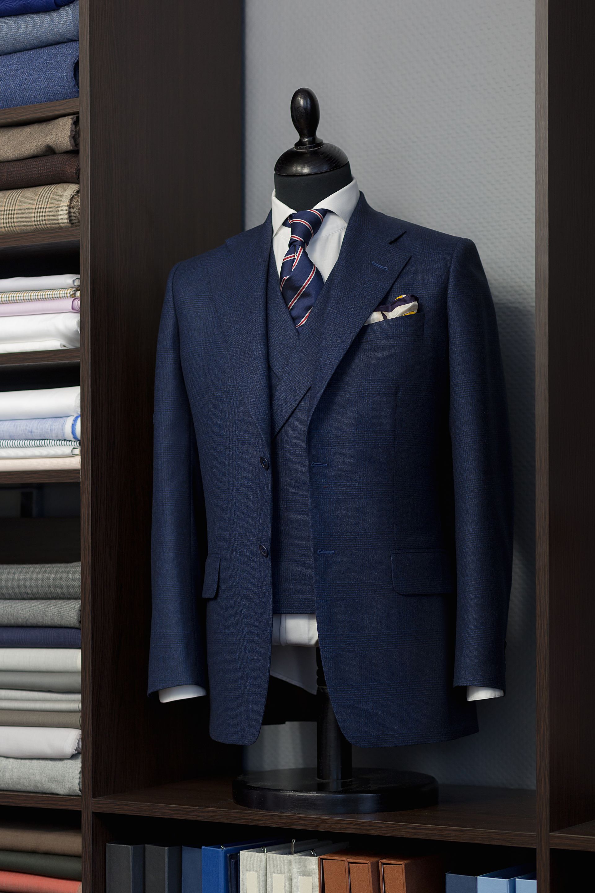 Blue suit on a mannequin in a closet, showing jacket, vest, shirt, tie, and pocket square.