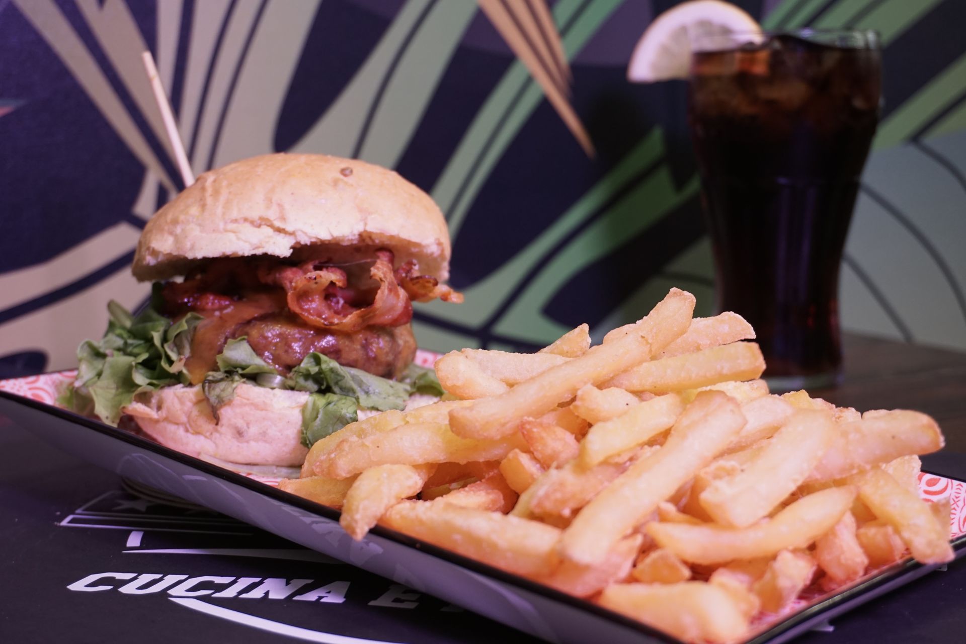 Un hamburger e patatine fritte su un piatto con una bevanda sullo sfondo.