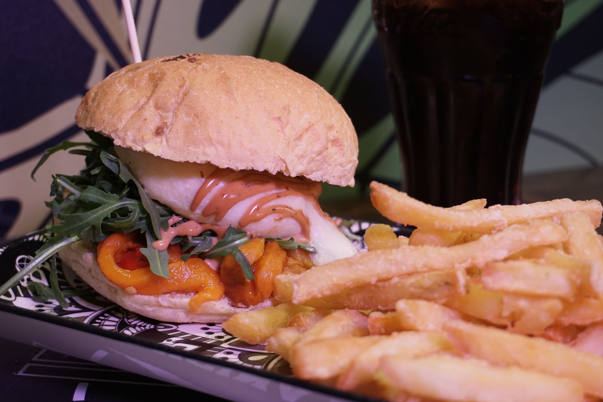 Un hamburger e delle patatine fritte sono su un piatto accanto a un bicchiere di soda.